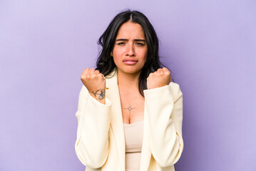 Young hispanic woman isolated on purple background showing fist to camera, aggressive facial expression.