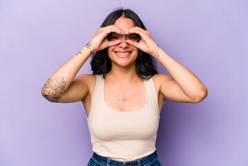 Young hispanic woman isolated on purple background showing okay sign over eyes
