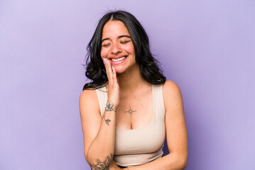 Young hispanic woman isolated on purple background laughs happily and has fun keeping hands on...