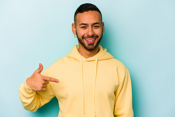 Young hispanic man isolated on blue background person pointing by hand to a shirt copy space, proud and confident