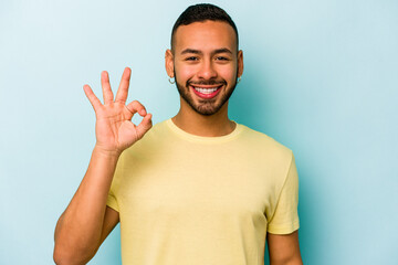Young hispanic man isolated on blue background cheerful and confident showing ok gesture.