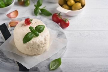 Ricotta cheese. Homemade Ricotta cheese with basil, garlic, tomatoes and green olives on parchment paperback and stand. Italian food. Selective focus.