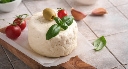 Ricotta cheese. Homemade Ricotta cheese with basil, garlic, tomatoes and green olives on parchment paperback and stand on old beige tiles background. Italian food. Selective focus.