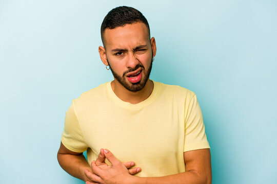 Young hispanic man isolated on blue background having a liver pain, stomach ache.