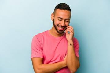 Young hispanic man isolated on blue background laughs happily and has fun keeping hands on stomach.