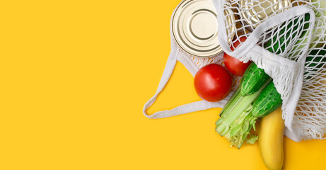 Delivery food, banner. Food items in a string bag on a yellow background. canned food, tomatoes, cucumbers, bananas. Donation, coronavirus quarantine. Food supplies for quarantine. Copyspace.