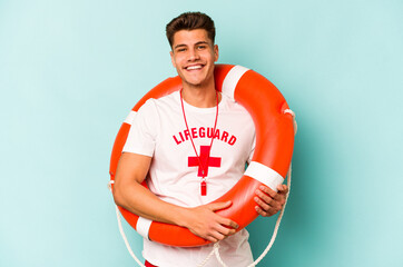 Young caucasian lifeguard isolated on blue background happy, smiling and cheerful. - obrazy, fototapety, plakaty