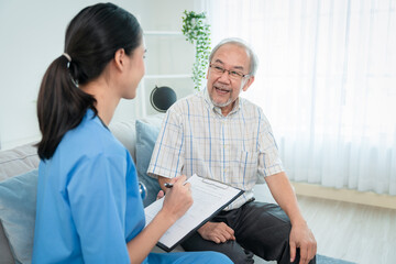 Asian young woman caregiver doctor give consultation and writing problem of elderly man patient in room during home visit
