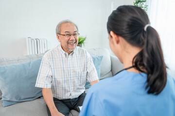 Obraz premium Asian elderly man patient smiling sit on sofa while young woman caregiver doctor give consultation about health in room during home visit