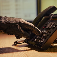 A man in black gloves at a landline phone dials a number, close-up. Office desk in a dark night...