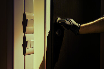 Man hand in a black glove opens the office door in the night light of a flashlight
