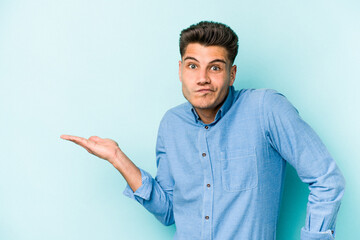 Young caucasian man isolated on blue background showing a copy space on a palm and holding another...