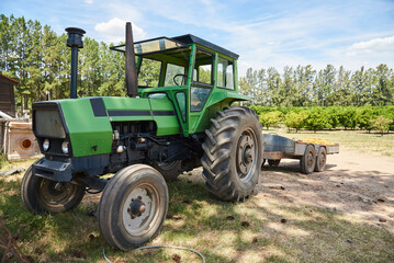 Green tractor next to an orange field during the summer.