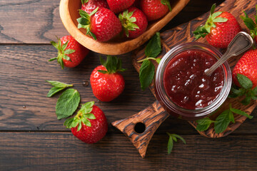 Strawberry jam. Strawberry jam in glass jar with fresh berries plate on an old wooden dark table background, closeup. Homemade strawberry fruity jam. Top view with copy space.