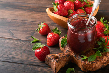 Strawberry jam. Strawberry jam in glass jar with fresh berries plate on an old wooden dark table background, closeup. Homemade strawberry fruity jam. Top view with copy space.