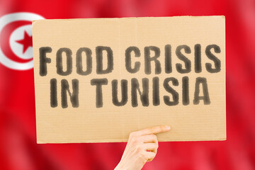 The phrase " Food crisis in Tunisia " is on a banner in men's hands with a blurred Tunisian flag in the background. Crisis. Finance. Life. Nutrition. Bread. Disaster. Collapse. Social issue
