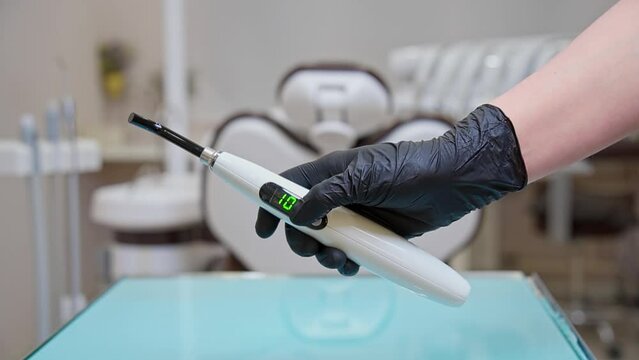 A dentist's assistant in black gloves shows how to work properly with a polymerization lamp in a medical office. A lesson for dentists and their assistants.