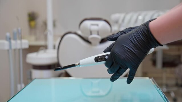 A dentist's assistant in black gloves shows how to work properly with a polymerization lamp in a medical office. A lesson for dentists and their assistants.