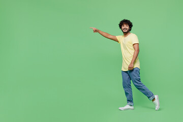 Full body young smiling happy Indian man 20s wearing basic yellow t-shirt walk going strolling...
