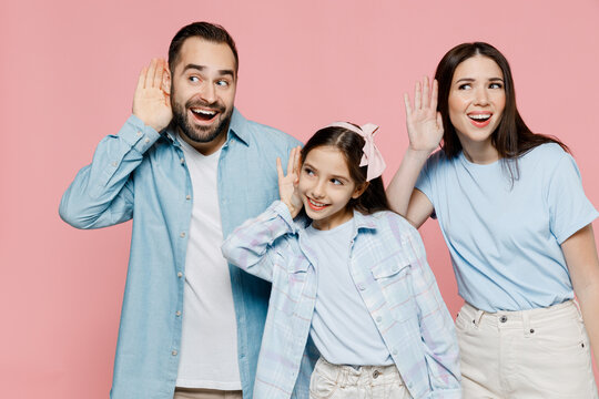 Young happy curious parents mom dad with child kid daughter teen girl in blue clothes try to hear you overhear listening intently isolated on plain pastel light pink background. Family day concept.