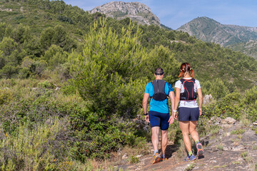 Rear view of two mountain runners through a forest on a sunny summer day.