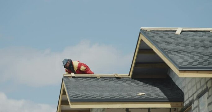 The builder is working on the roof of the house - laying shingles
