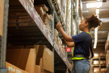 African American purchasing worker wearing a uniform holding a digital tablet checks the inventory of raw materials in a warehouse.