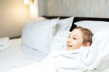 the child is resting on a large bed in a hotel room with his hands behind his head