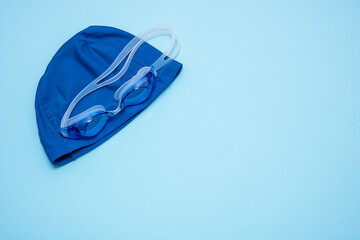 swimming cap and goggles on a blue background with copy space