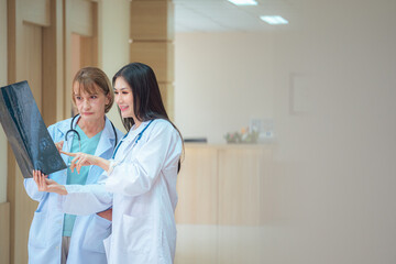 Young beautiful female doctor look at X-ray scan consult,diagnosis,discuss patient's log to senior doctor while walk in hospital hallway. Two different generation diversity multiracial medical concept
