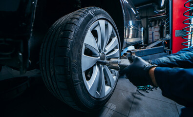 Hands of professional car mechanic changing car wheel in auto repair service. Close up