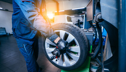 Auto mechanic uses tire balancing machine and turning tire - obrazy, fototapety, plakaty