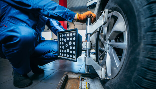 Auto mechanic installing sensor during suspension adjustment and automobile wheel alignment work at repair service station. Close up