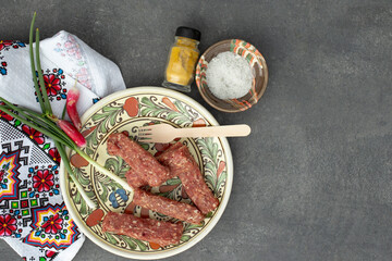 Mititei or mici on a plate, ready for grill on a grey tile background