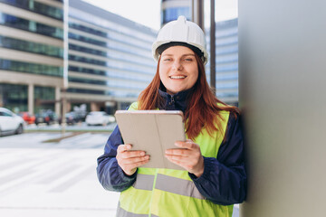 Smile Young architect woman in white hardhat and safety vest using digital tablet outdoors. Female...