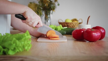 Close-up of an unrecognizable woman's hand cutting a carrot with a kitchen knife. Cooking in the kitchen.