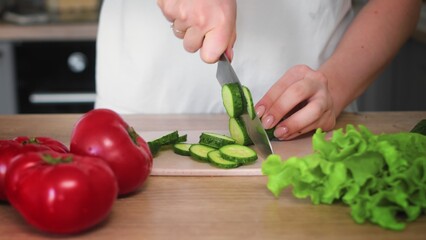 Close-up of an unrecognizable woman's hand cutting a cucumber with a kitchen knife. Cooking in the kitchen.