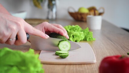 Close-up of an unrecognizable woman's hand cutting a cucumber with a kitchen knife. Cooking in the kitchen.