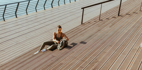 Pretty young woman takes a break after running in urban area