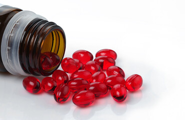 Red transparent oval capsules with vitamins with a dark glass bottle. On a white background....