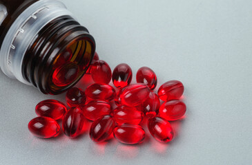 Red transparent oval capsules with vitamins with a dark glass bottle. On a grey background. Selective focus.
