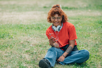 african american girl with mobile phone and headphones on grass field