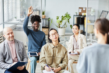 Portrait of young black man raising hand asking question during educational seminar in office, copy...