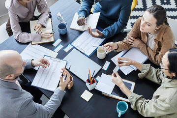 Top view at diverse group of people at meeting table in office setting communicating and gesturing