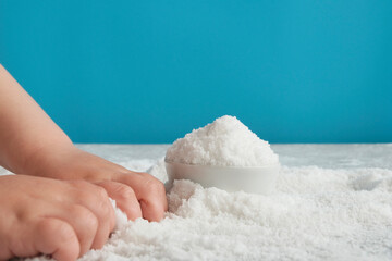Close-up of the baby's hands, which deals with bulk material, hand motility, sand or sugar, salt. Lack of food, without infant formula. Blue background. The table is light.