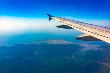 View from the airplane window at a beautiful blue clear sky, earth, sea and the airplane wing