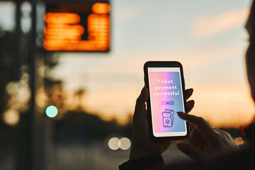 Woman buying ticket online near bus stop. Person paying for ticket using mobile payment app. Buying service on the go. Order confirmation on mobile screen - obrazy, fototapety, plakaty