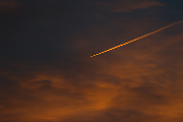 Un avión cruza el cielo en pleno atardecer dejando una estela brillante de luz naranja