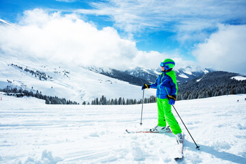 Fototapeta na wymiar Boy stand on ski track in sport outfit observing the mountain