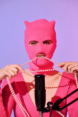 Unrecognizable young female influencer wearing stylish pink sweater and balaclava sitting in front...